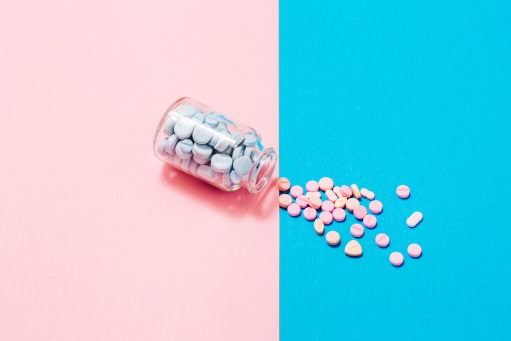Pink pills spill out of a bottle on a split-screen blue and pink background.