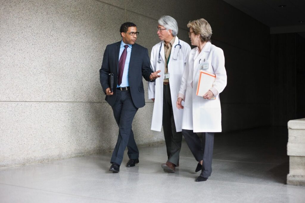 A businessperson converses with two doctors as they walk through a building lobby.