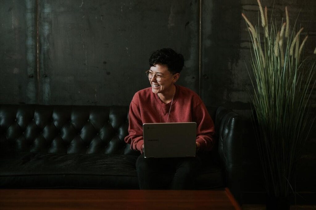 A photo of a 20-something student sitting on a couch with a laptop, laughing and looking away from the camera.
