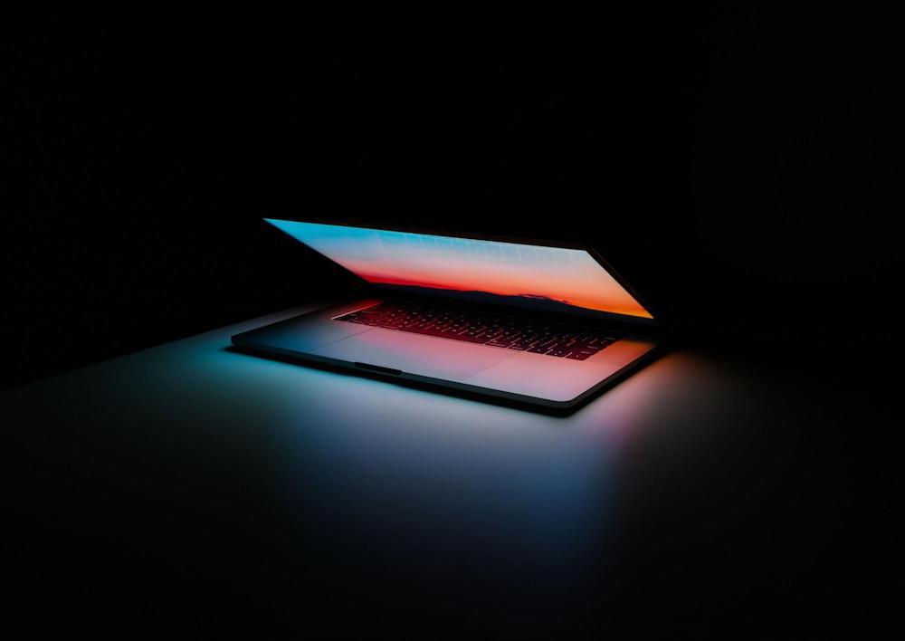 A computer opens halfway and lights up in a dark room.