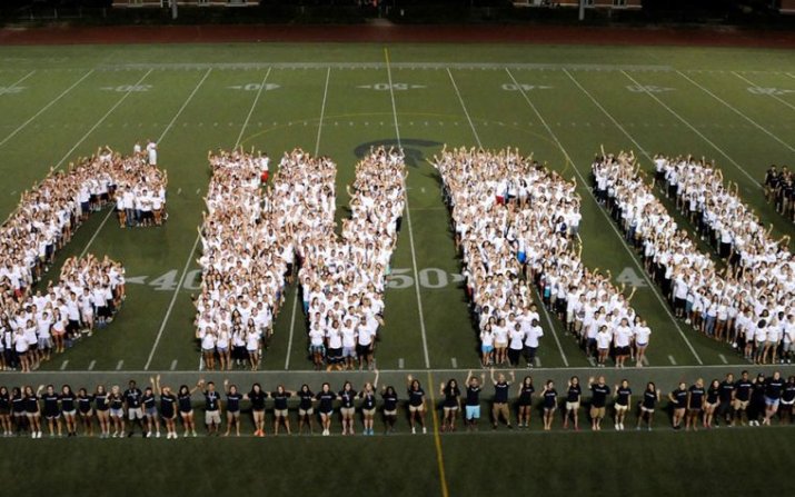 Students wearing white stand in a formation that spells out "CWRU" on a football field.