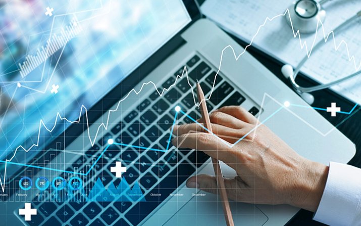 A closeup of a hand holding a pencil while typing on a laptop, overlaid by charts and graphs.