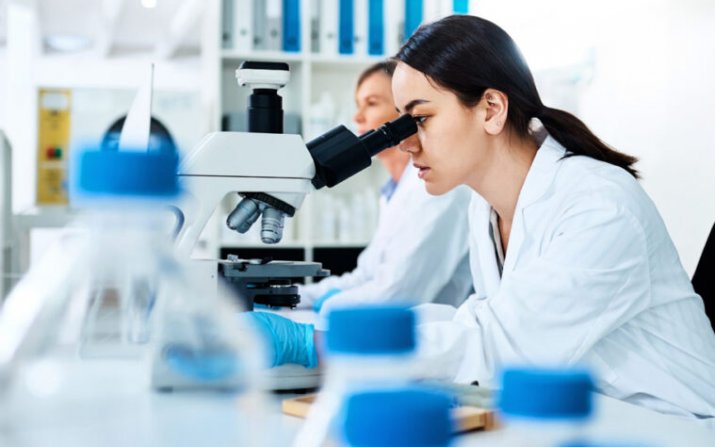 A woman in a lab coat looks through a microscope.