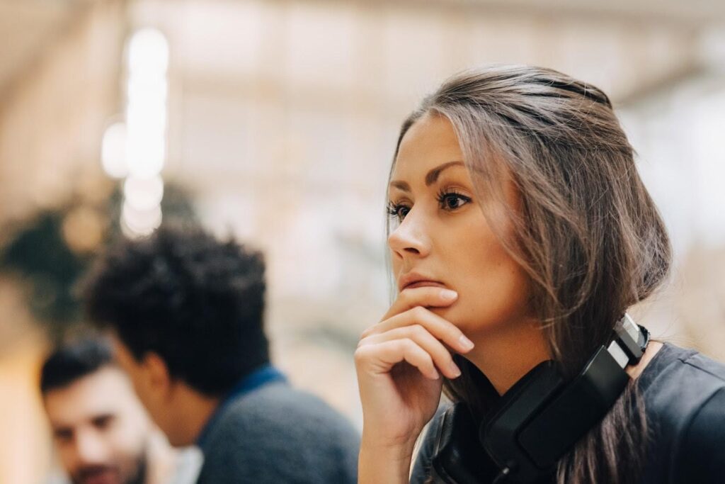 Close-up of the face of a woman in thoughtful repose; her position and the headphones around her neck suggest she is looking at a computer screen.